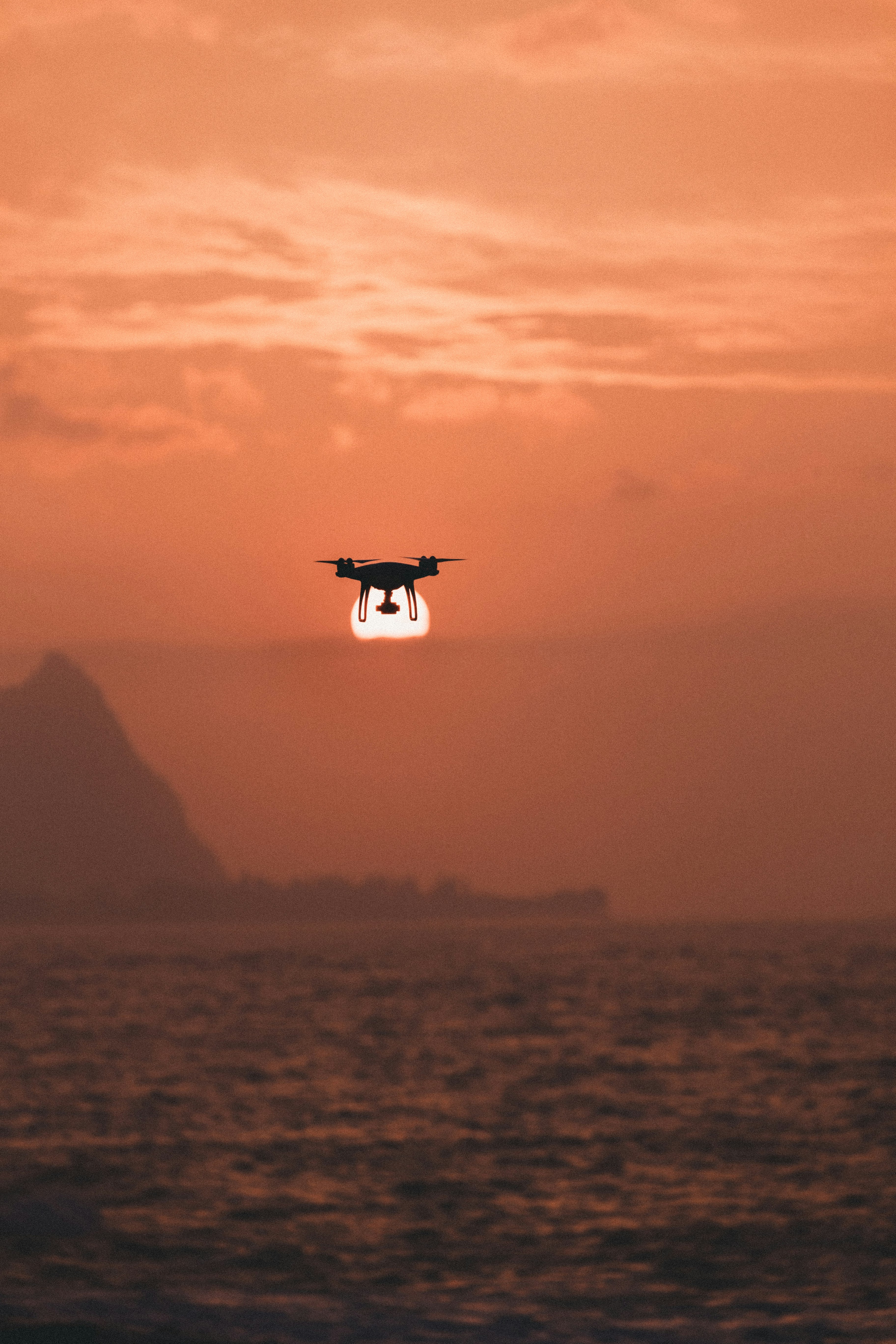 silhouette of drone hovering above body of water